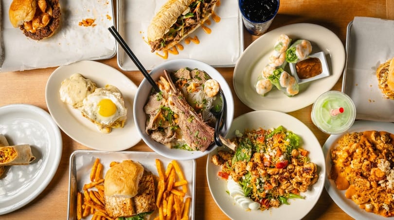An overhead view of a table laden with various dishes, including sandwiches, pho, spring rolls, and salads.