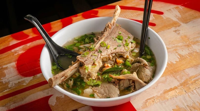 A large bowl of pho with a prominent beef rib, other cuts of meat, and herbs.