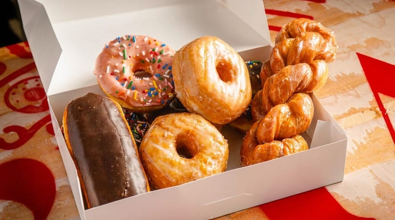 Assorted donuts, including glazed, chocolate, and sprinkle varieties, in a white box.