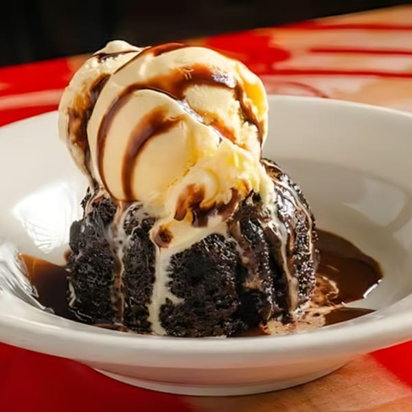Chocolate lava cake with vanilla ice cream and chocolate syrup in a white bowl.