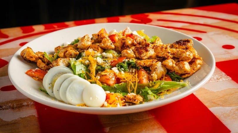 A vibrant salad with grilled chicken, sliced hard-boiled eggs, lettuce, tomatoes, and shredded cheese.