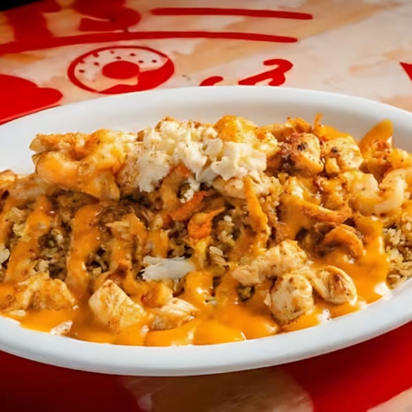 A white plate filled with rice, shrimp, chicken, and crab meat, drizzled with cheese sauce.