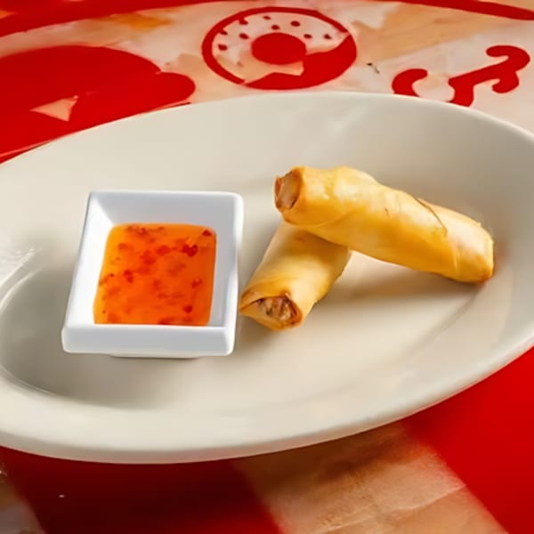 Two crispy spring rolls and a small dish of sweet chili dipping sauce on a white plate.